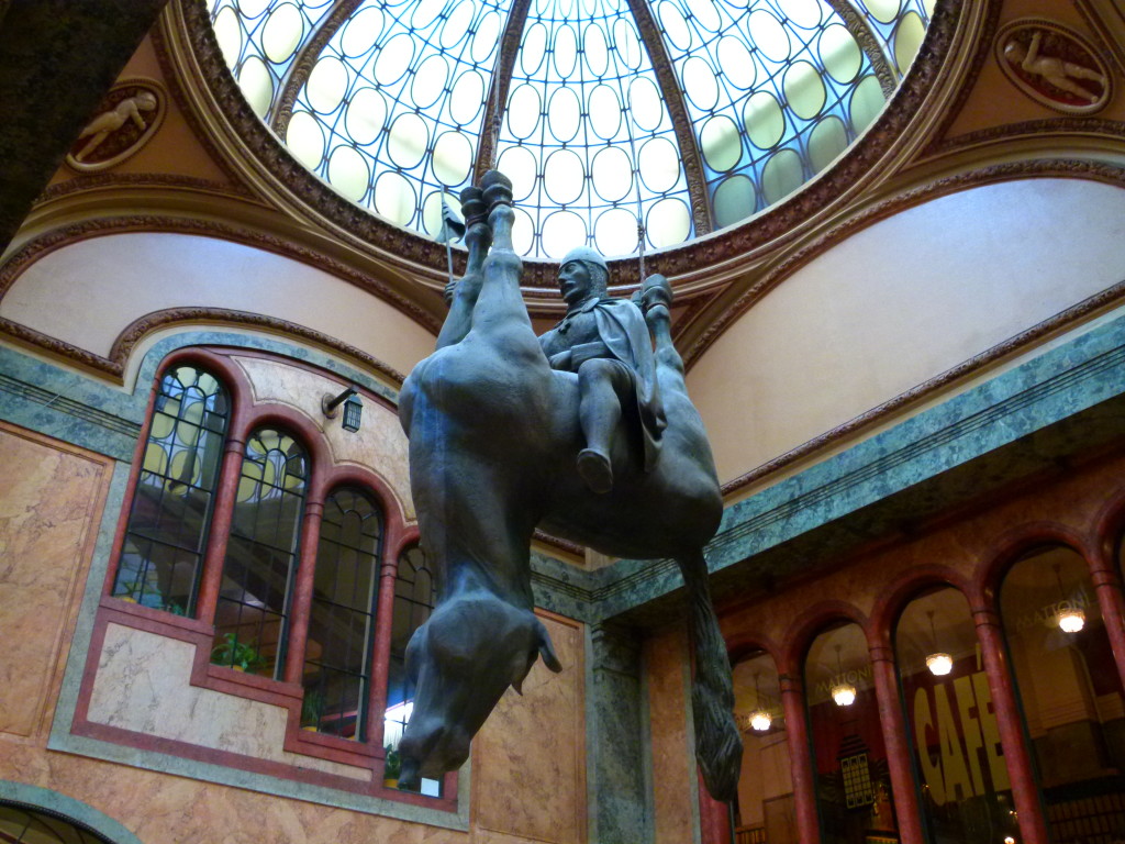 Hanging from the ceiling of the Art Nouveau Lucerna Palace in Prague, an ancient king rides triumphantly astride... an upside-down, apparently dead horse. Created by Prague-born artist David Cerny.